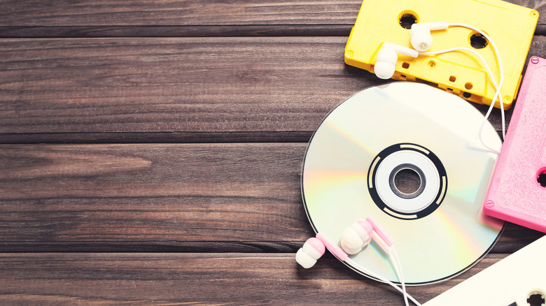 CDs and pink and yellow cassette tapes on a wood surface