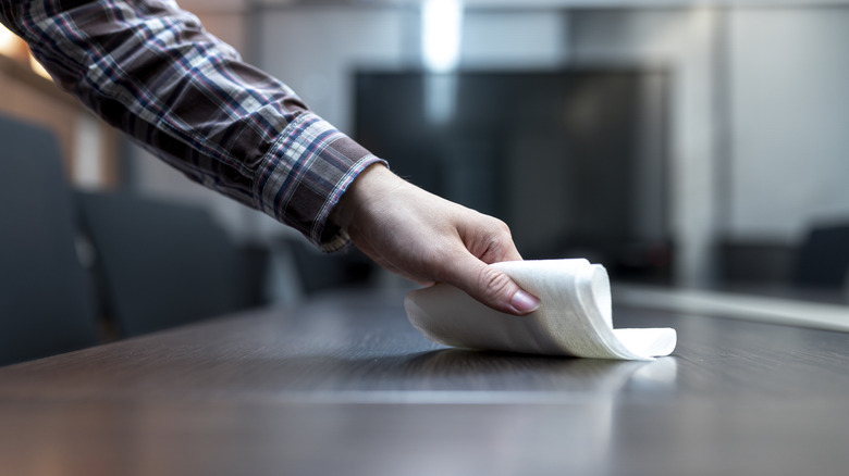 Person dusting a table with a white cloth