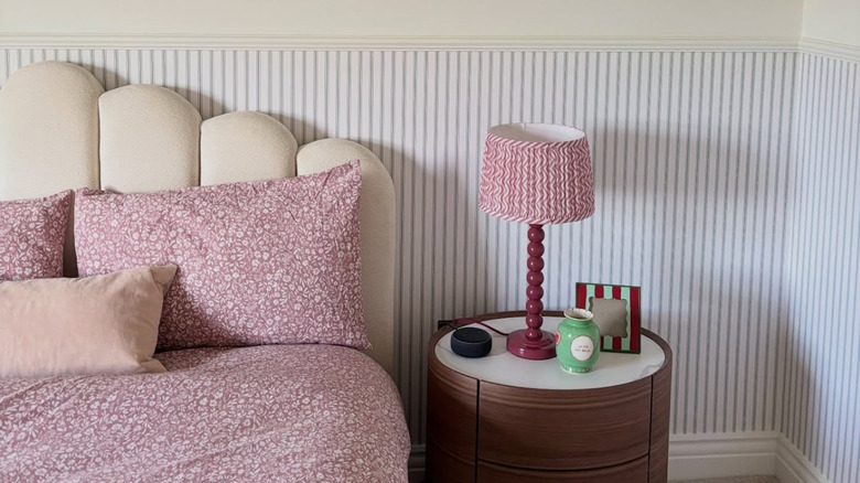 A bedroom with blue ticking stripe wallpaper, red floral bedding, and a brown table
