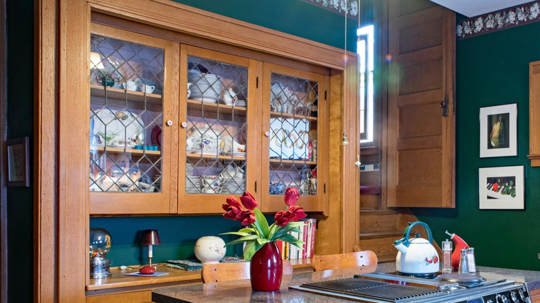 A kitchen with hunter green walls and a large wooden china cabinet to house plates and cutlery