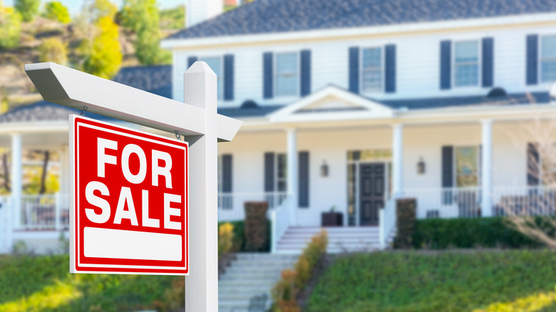 A for sale sign in a white house's front yard
