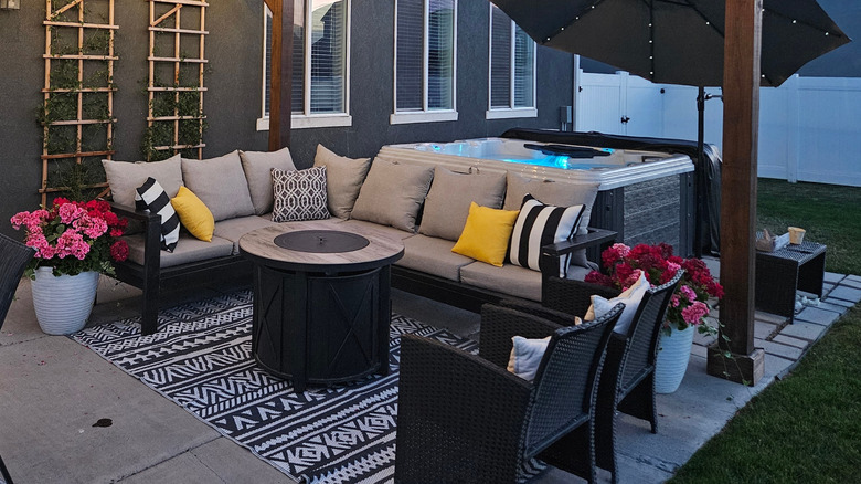 An outdoor patio set behind a single family home is illuminated by a band of lights strung across a wooden covering.