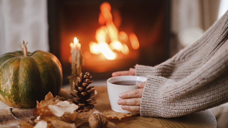 Person holding a mug on a table with fireplace in the background