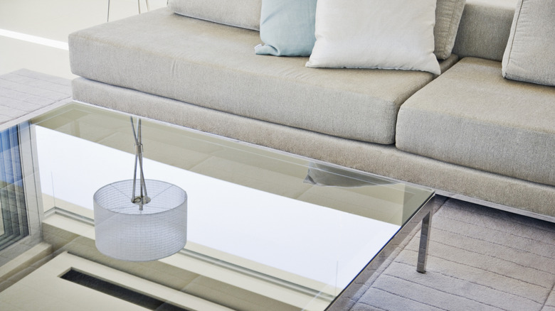 A large mirrored coffee table in a living room reflects a lamp