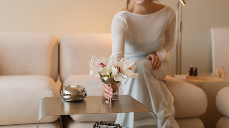 A woman places a mirrored vase with flowers on a small coffee table