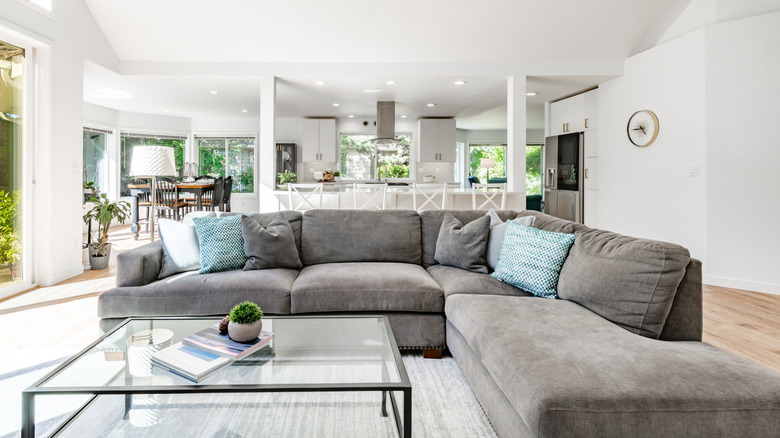 Living room with glass coffee table in the middle of a gray, oversized L-shape couch.