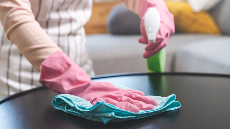 rubber gloved hands cleaning with cloth and cleaning product