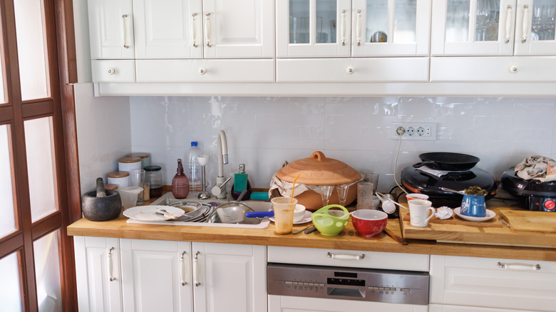 A messy kitchen counter with cluttered cups and dirty dishes