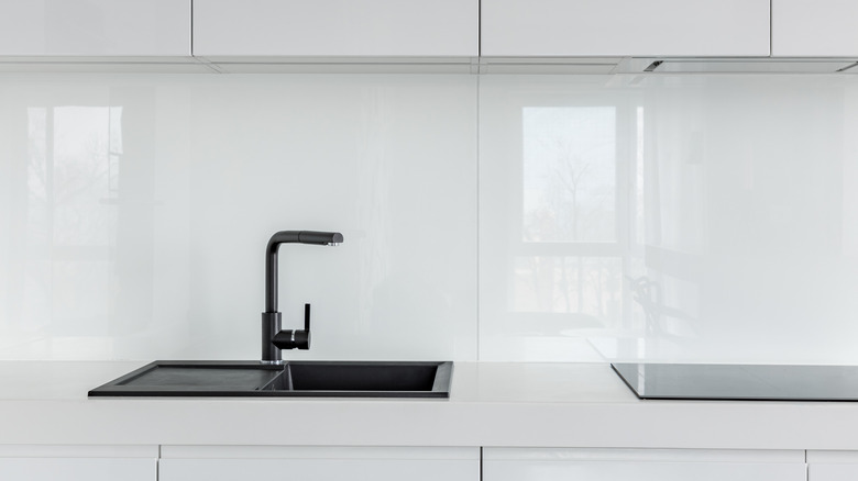 A white kitchen with a black sink and faucet and a glass backsplash