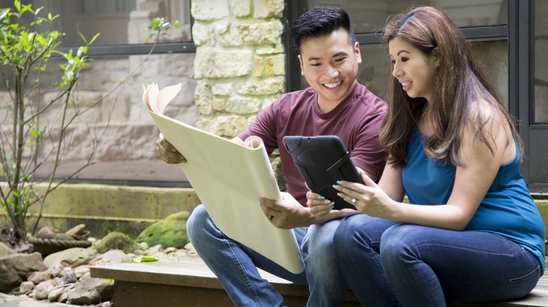 A landscape designer and their client sit in a backyard discussing plans.