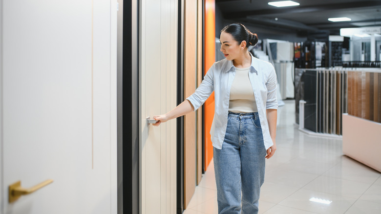 Woman in a door showroom opens a white door with metal hardware.