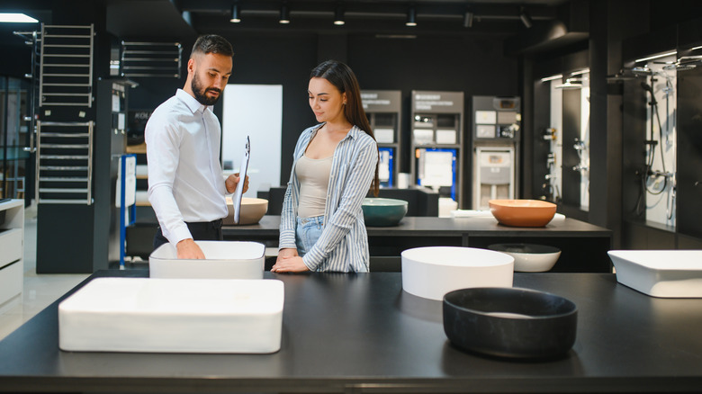 Worker showing client different sink basins in showroom