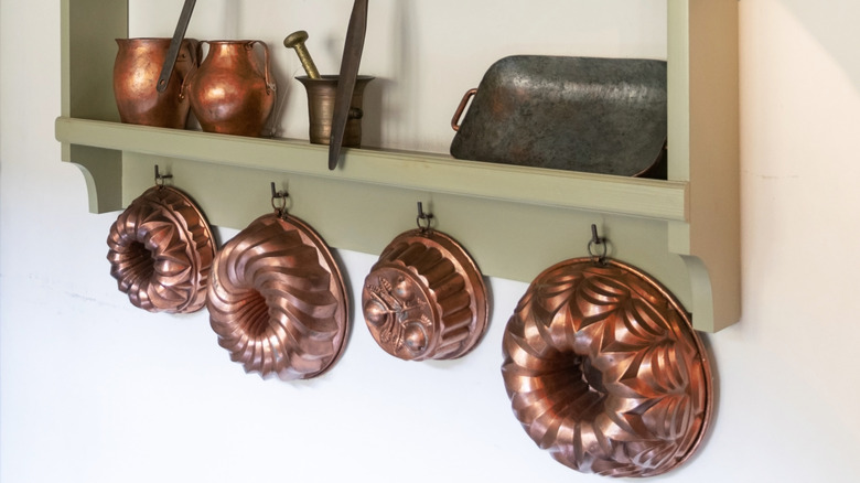 Copper cake molds hanging from hooks on shelf