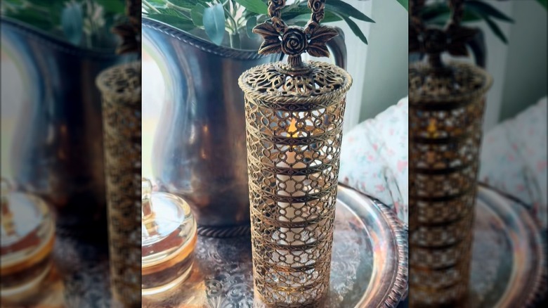 An LED taper candle glows beneath a vintage metal hairspray cover.