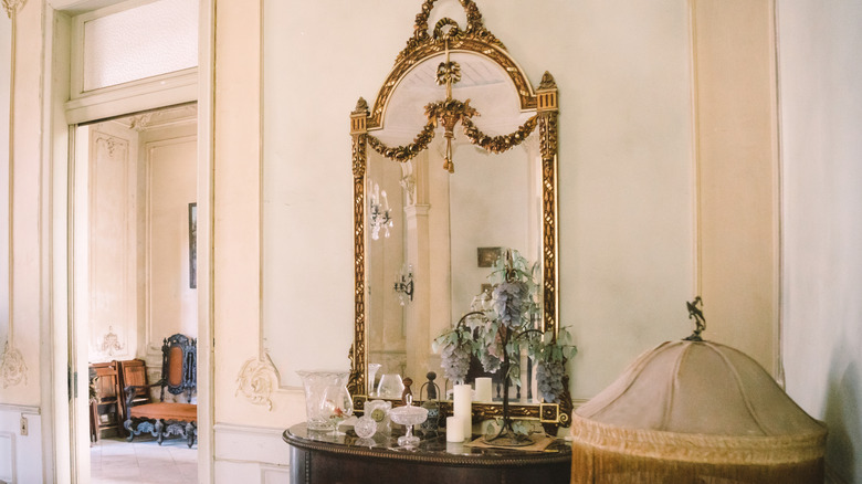 A large gilded mirror against a wall behind a small table full of decor