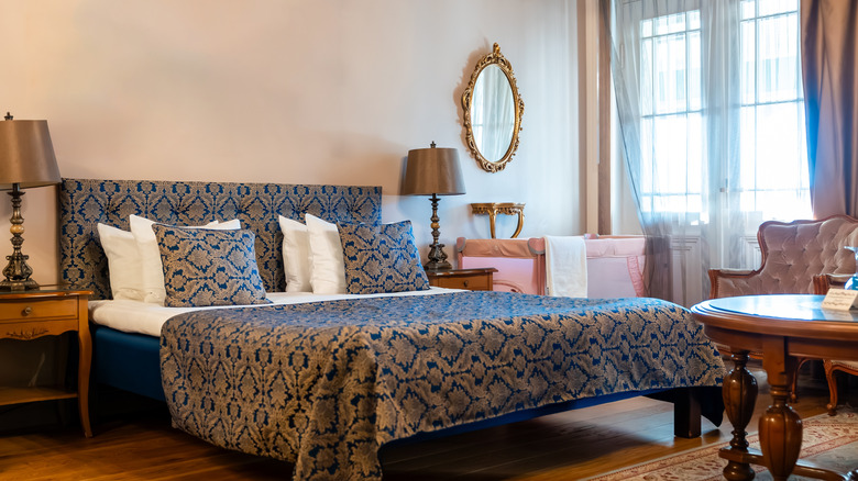 A bedroom with beautiful decorative bedding, elegant wood furniture, and a gilded mirror