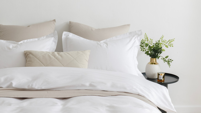 A bed with white sheets with beige accents