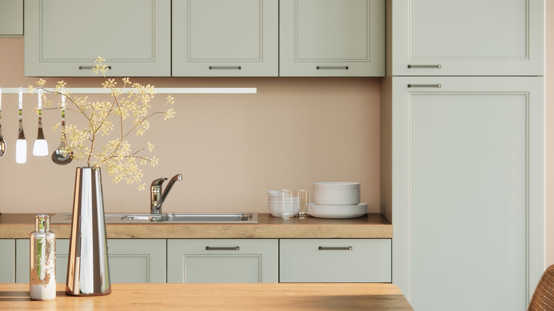 A kitchen with light green cabinets, a wood countertop, and metal decor