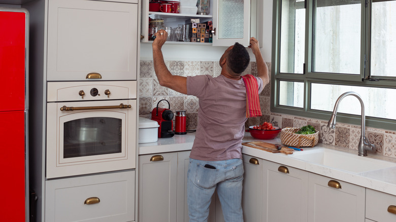 Man looking into full kitchen cabinet