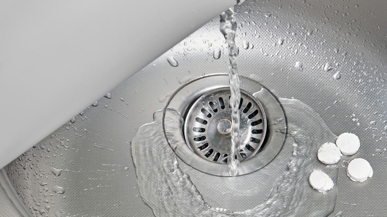 A black rubber stopper on a chain partially covering a sink drain.