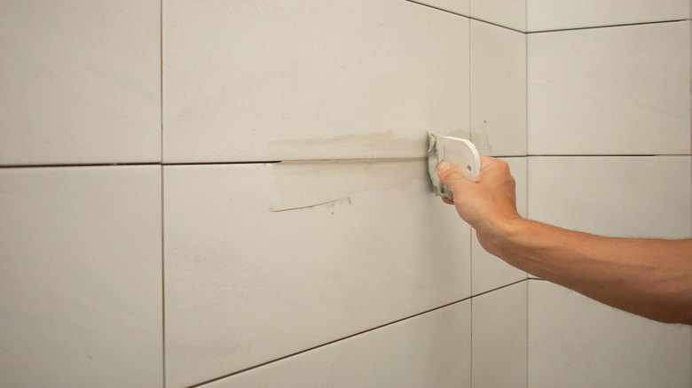 A hand adds grout to large-format shower tiles