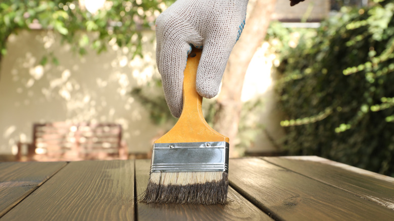 Man applying wood stain onto wooden surface outdoors, closeup