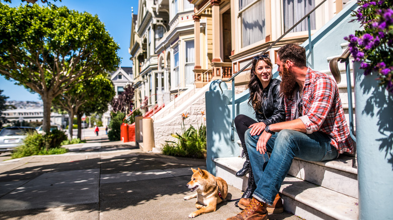 Couple seated on a stoop and dog lying down in a walkable neighborhood