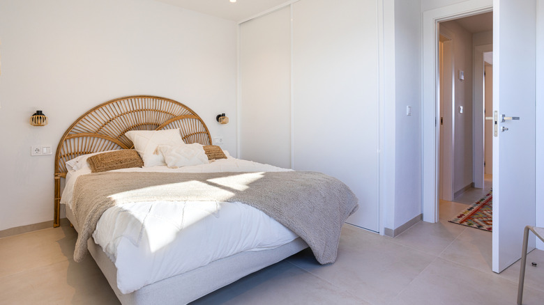 A bed with a curved rattan or cane headboard inside a modern minimalist bedroom.