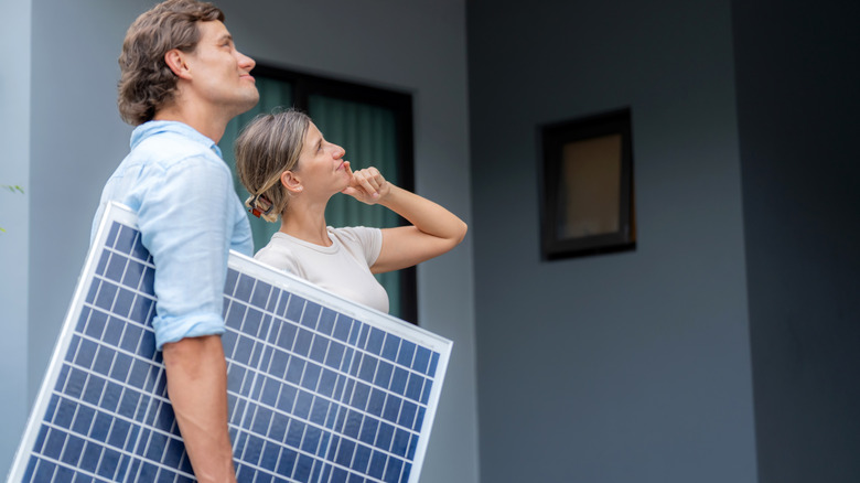 A couple is holding a solar panel in front of a house