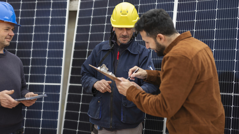 Man signing a contract while contractors stand in front of solar panels