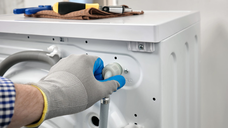 A hand disconnecting water supply hose from washing machine