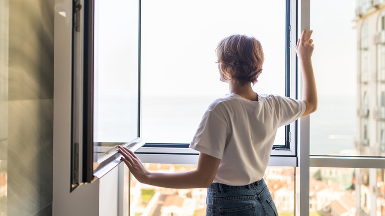 Person looking out open window in home