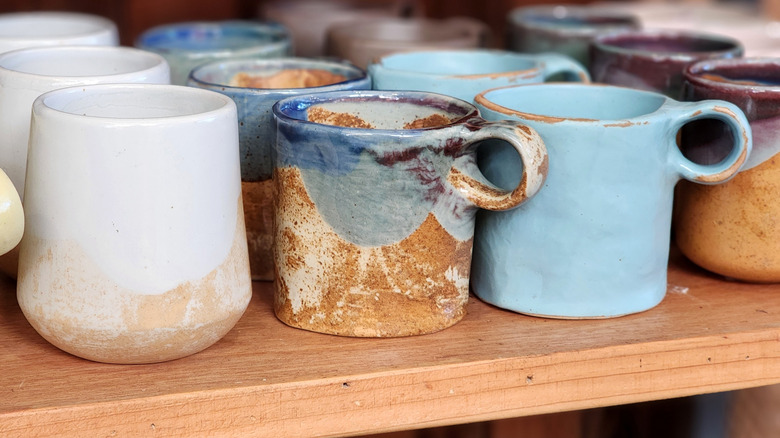 A shelf holds various mugs in blue and white and mixed colors.