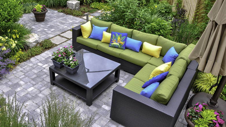 small patio with L-shaped sofa, throw pillows, greenery, and glass table
