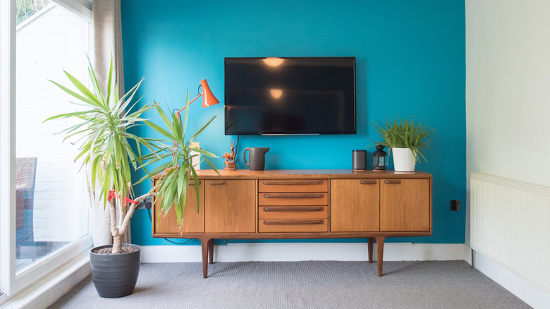 blue-painted feature wall of a living room with a television hanging over a wooden console table