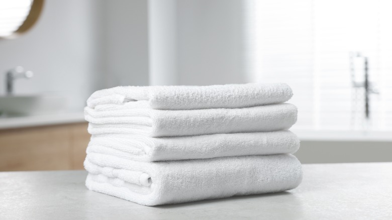 A stack of white bathroom towels that will needed to be hung properly after a shower.