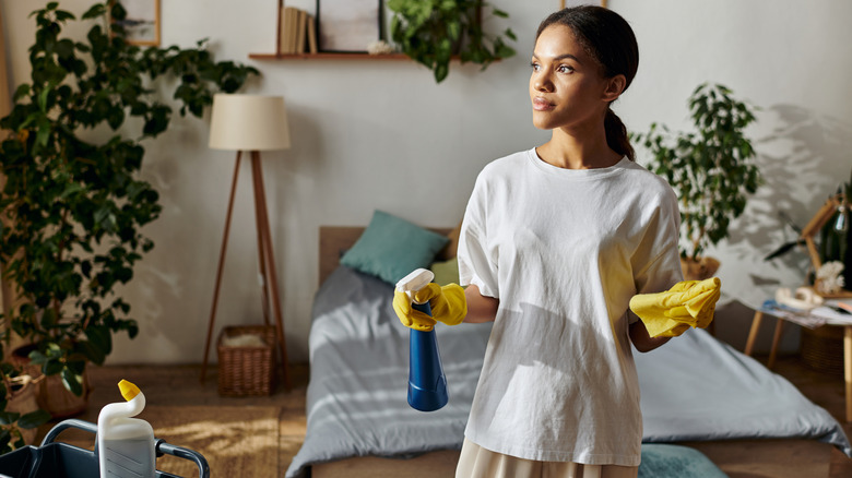 A woman wearing yellow gloves holding a spray bottle in one hand and a clean cloth in the other