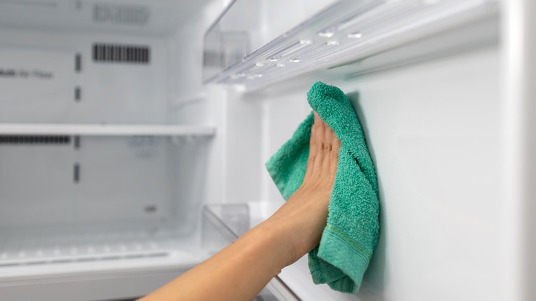 Someone wiping fridge interior with a microfiber cloth