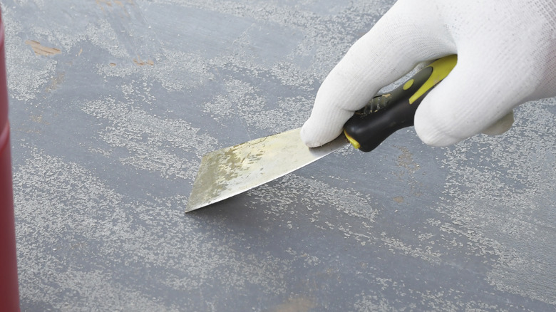 A hand with a white glove using a scraper to remove grey paint.