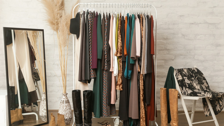 Clothing rack with lots of coats and shoes beside a full length mirror