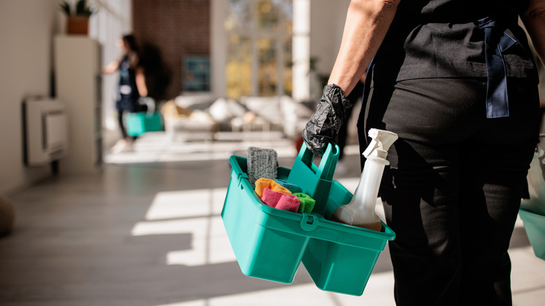 Professional cleaner carries caddy of cleaning supplies through modern home