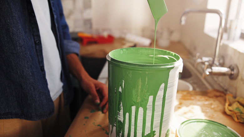 Person dipping paint brush in green paint can on top of kitchen counter.