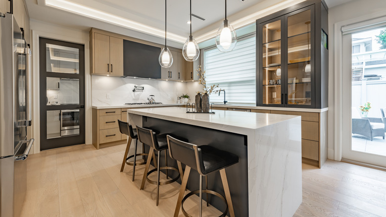 Modern kitchen with brown and gray cabinets, island with stools, and white countertops.