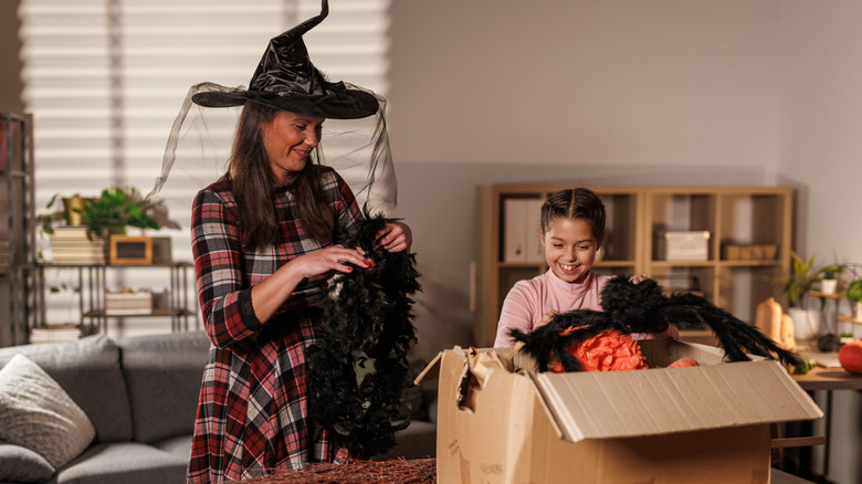 Woman wearing a witch's hat while young girl goes through a box of Halloween costumes