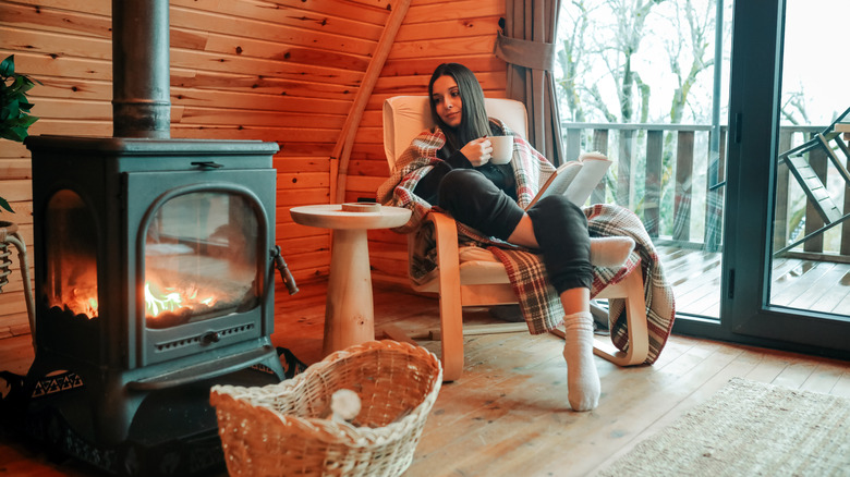 Young woman relaxing with a book in front of a cozy fireplace in a neat home