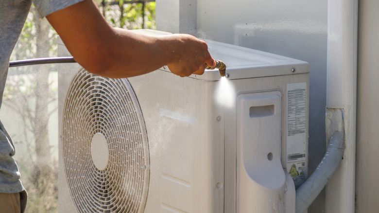 Person using a high-pressure washer to clean the outdoor air conditioning unit