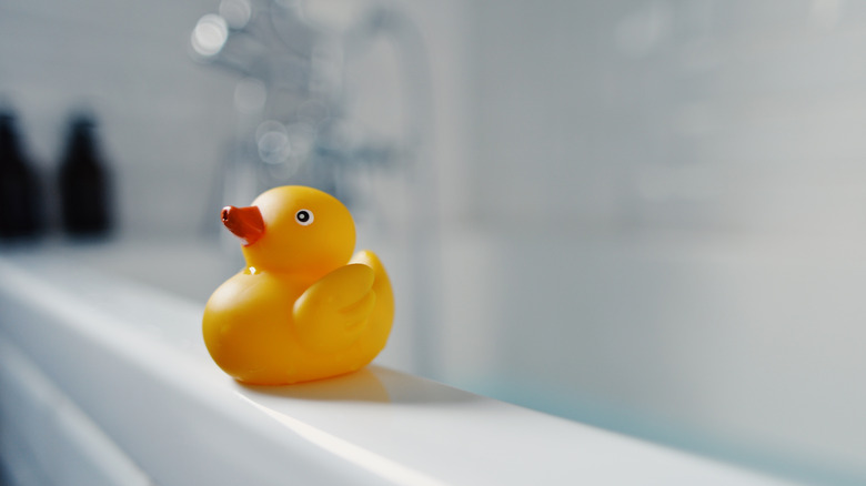 Yellow rubber duck on edge of white bathtub