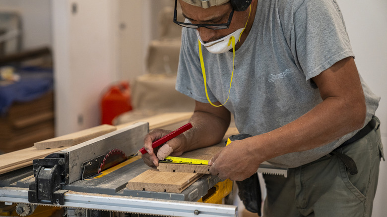 A wood flooring contractor measures a board before cutting it on an electric saw
