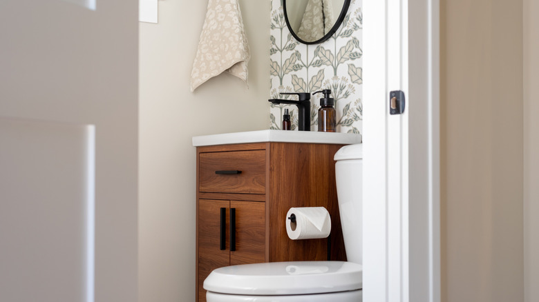 A very compact bathroom with toilet and sink next to each other and beige, white and wood tones