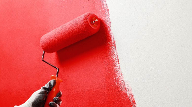 Hand holding roller brush painting a white wall red.